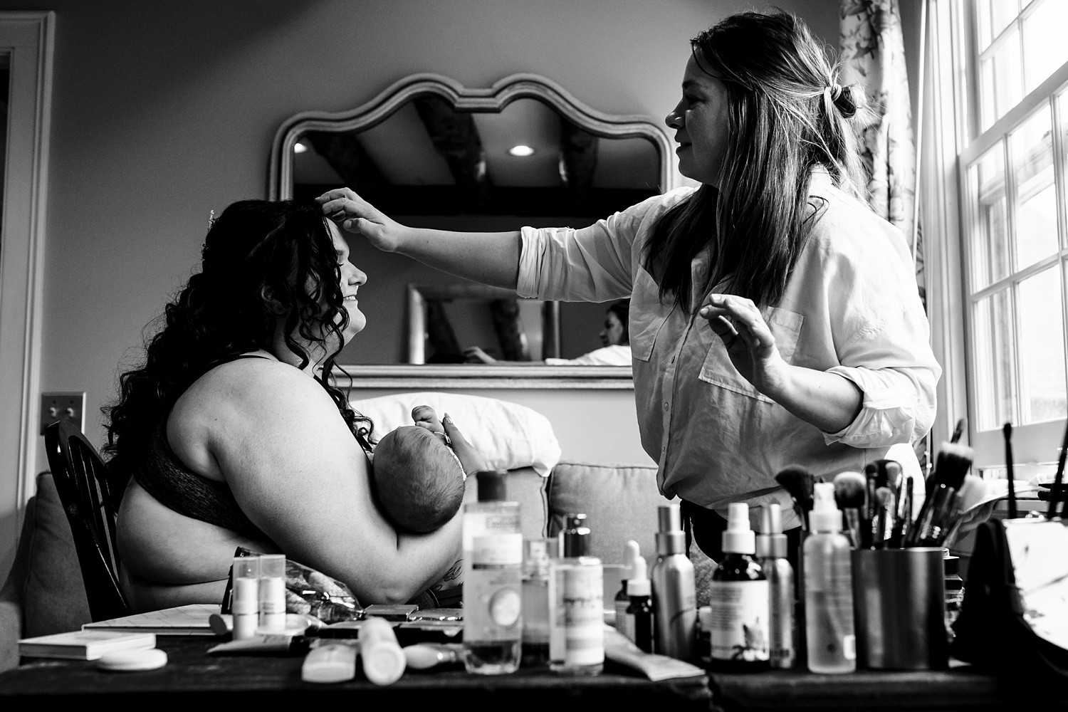 The bride gets her hair touched up while holding her son