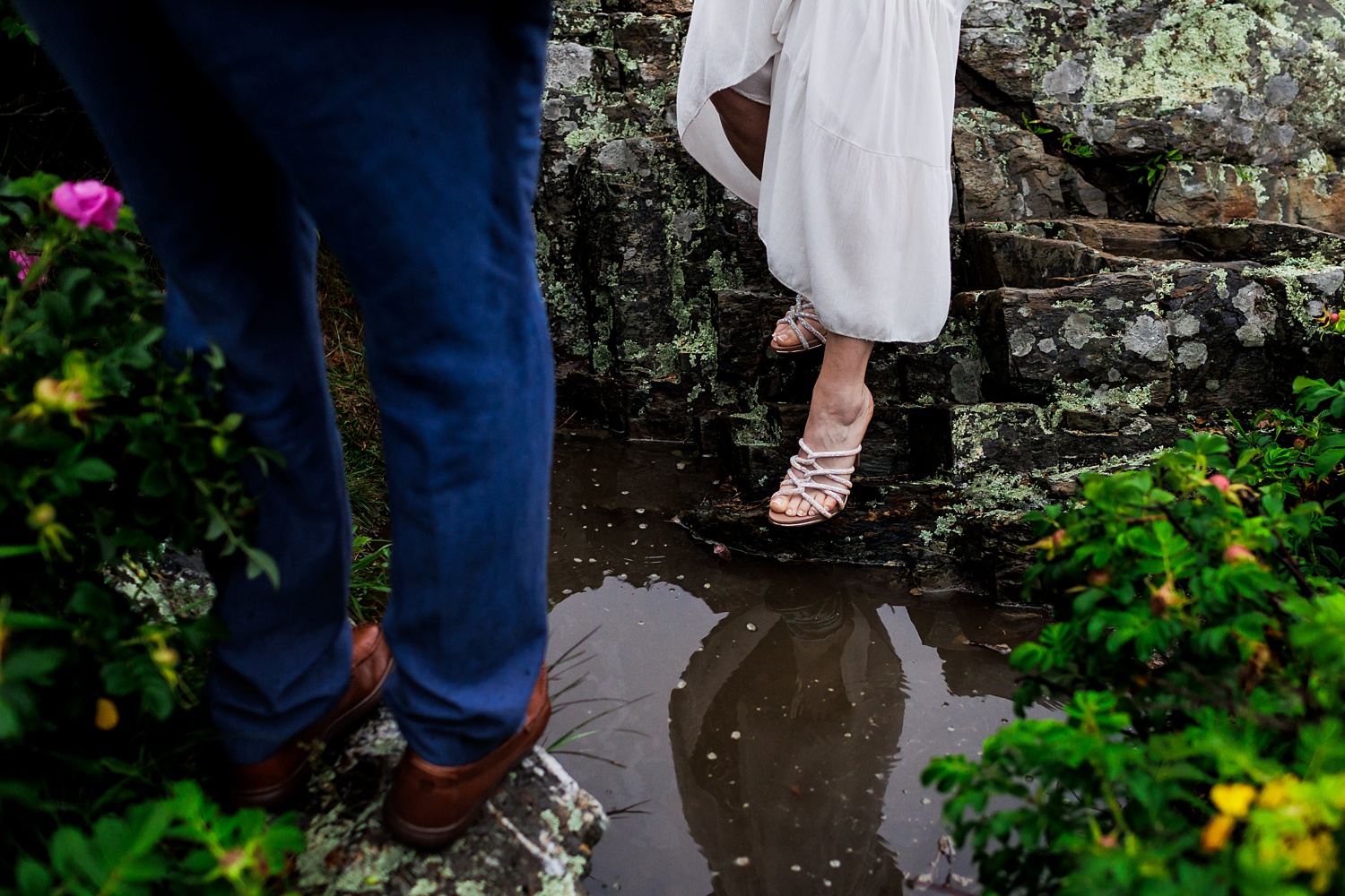 The groom helps the bride over a puddle on their rainy Marginal Way Maine elopement